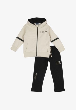 Felpa leggera beige chiaro con dettagli neri e testo "POWER", abbinata a pantaloni della tuta neri con il testo "CHANGE" e "SUCCEED" in oro.
