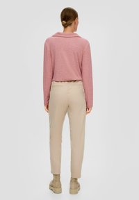 Różowa bluzka z długim rękawem i bez kołnierza zestawiona z beżowymi, zwężającymi się spodniami oraz jasnymi botkami do kostek, widok z tyłu.