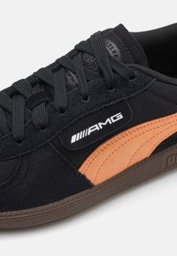 Baskets en daim noir avec accents orange et semelle en caoutchouc texturée. Comprend des lacets noirs et un logo AMG sur le côté.