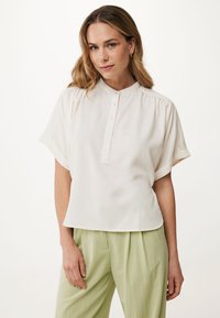 Blusa bianca a maniche corte con colletto alto e cinque bottoni sul davanti. Tessuto morbido con una texture liscia e vestibilità comoda.