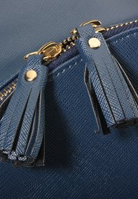 Borsa a tracolla blu con texture, caratterizzata da una zip dorata e due pendenti blu. Il materiale sembra resistente con una finitura grezza.