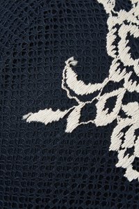 Tela texturizada azul marino con intrincados bordados florales blancos. El diseño presenta detalles delicados sobre un fondo cuadriculado.