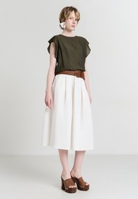 Top corto a maniche, di un verde oliva testo abbinato a una gonna bianca plissè, accentuata da una cintura intrecciata marrone e scarpe platform marroni.