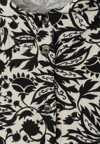 Chemise col avec imprimé floral noir sur fond crème, avec trois boutons foncés visibles le long du centre devant.