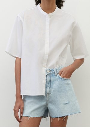 Person wearing a white short-sleeve button-up shirt and light blue high-waisted denim shorts with one hand in pocket.