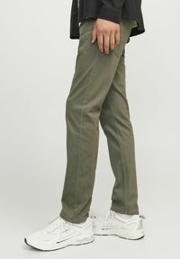 Pantaloni verde oliva con vestibilità dritta, realizzati in cotone. Abbinati a scarpe da ginnastica bianche, con tomaia in rete texturizzata e dettagli neri.