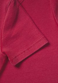 Elegant material roșu, cu textură bătătură, arătând un manșon pliat și o parte din corp. Cusăturile sunt vizibile, subliniind textura materialului.