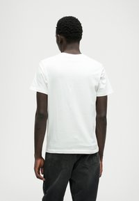 T-shirt branca de algodão com mangas curtas, decote redondo e um corte descontraído. Textura suave, sem padrões visíveis ou detalhes, combinada com jeans escuros.