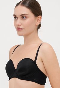 Sort polstret bh med underwire og en glat satinfinish, justerbare stropper og et kurvet design, der har et lille logo på siden.