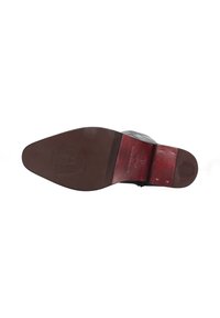 Suela de zapato de cuero marrón con forma puntiaguda, que presenta un patrón texturizado y un acento rojo contrastante cerca del talón. Detalle destacado del logo en relieve.