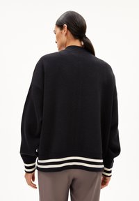 Zwarte oversized trui met een geribde kraag en gestreepte zoom. Zachte textuur, relaxte pasvorm en brede mouwen. Geschikt voor casual kleding.