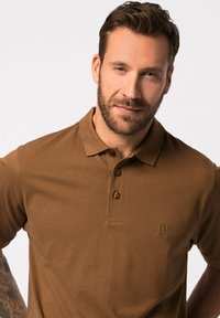 Hnědá polo košile z bavlněné směsi s límečkem, tříknoflíkovým zapínáním a vyšívaným logem na hrudi. Hladká textura a přiléhavý střih.