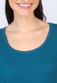 Türkisfarbener gestrickter Oberteil mit einem gekerbten Ausschnitt und kleinen Lochmusterungen. Weicher Stoff, geeignet für die Freizeit.