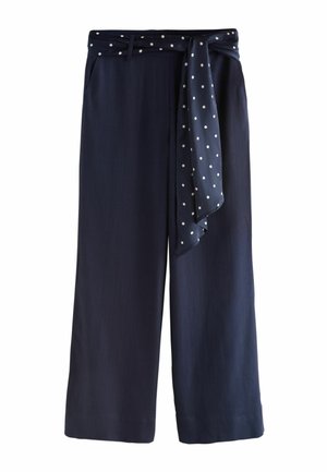 Marineblauwe broek met wijde pijpen en een bijpassende gestipte stoffen riem gestrikt rond de taille, met riemlussen en voorzakken.