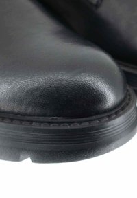 Scarpa in pelle nera con punta arrotondata, superficie liscia e suola in robusto gomma nera che presenta un bordo texturizzato e leggere incisioni.