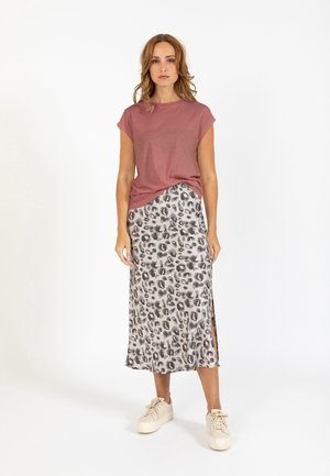 Donna in piedi che indossa una maglietta a maniche corte color malva, gonna midi con stampa leopardata e spacco laterale, e sneakers piattaforma bianco sporco su sfondo bianco.