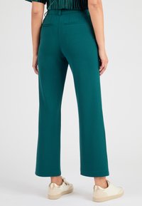 Teal wijde broek met een gladde textuur, voorzien van twee achterzakken en een medium taille. Gecombineerd met witte schoenen met gouden accenten.