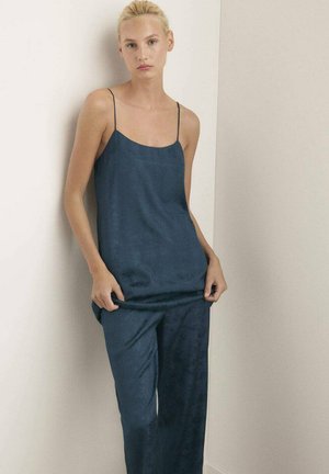 Camisón de seda azul y pantalones a juego con un patrón sutil. El camisón presenta tirantes finos y un corte holgado, mientras que los pantalones son de pierna recta.