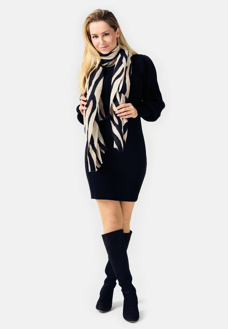 Knit black dress with ribbed texture, paired with a two-tone scarf featuring black and tan stripes. Knee-high black suede boots.