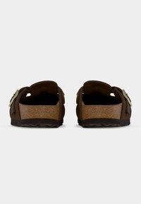 Καφέ σανδάλια που φοριούνται εύκολα με πάτο από φελλό, καφέ υφή στην επάνω επιφάνεια και διπλά ρυθμιζόμενα λουράκια με μεταλλικές λεπτομέρειες σε κάθε πλευρά.