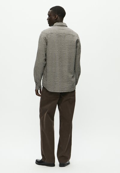 Chemise à carreaux noir et blanc avec col, manches longues et coupe décontractée, assortie avec un pantalon marron. Tissu lisse avec des lignes verticales.