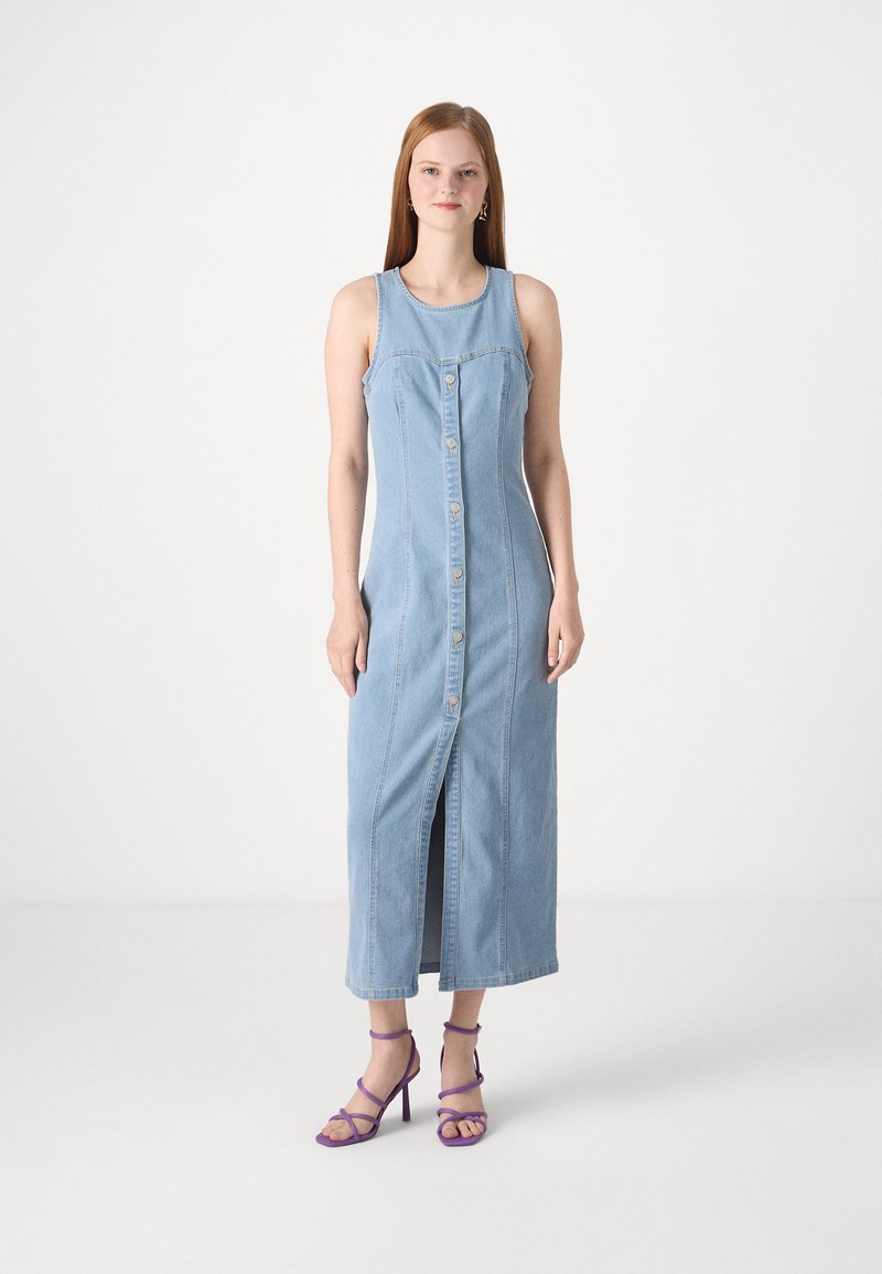 Lyseblå denim maxi-kjole med frontknaplukning, sideslids og ærmeløs design, parret med lilla remsandaler med høj hæl.