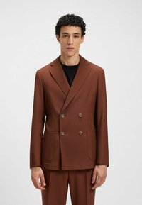 Brauner, doppelt geknöpfter Blazer mit zwei Vorderaschen, strukturiertem Stoff, Reverskragen und Knopfakzenten, kombiniert mit passenden Hosen.