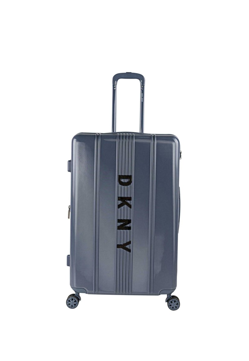 Maleta dura gris con diseño acanalado vertical, asa retráctil, cuatro ruedas y logo de DKNY en negro en la parte frontal.