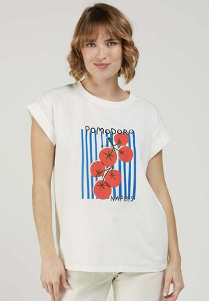 Jeune femme aux cheveux courts et ondulés portant un t-shirt blanc ornée d'un graphisme de tomates rouges et de rayures verticales bleues avec le texte « Pomodoro Naples ».
