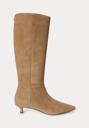 Botte haute en daim beige avec bout pointu et petit talon kitten, vue de côté sur un fond uni.