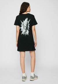 Robe t-shirt noire avec un graphique de mains jointes ornées de perles, sur un fond éclatant. Manches courtes, coupe décontractée, en coton.