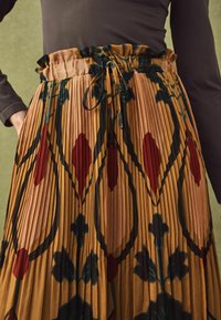 Pleated skirt featuring a floral pattern in earthy tones of orange, red, and green, with a ruffled waistband and drawstring.