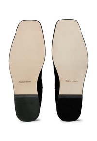 Suela de zapatos de ante negro con una parte inferior lisa de color beige. Cuenta con un sello de la marca "Calvin Klein" y un tacón de goma negra con textura para mayor agarre.