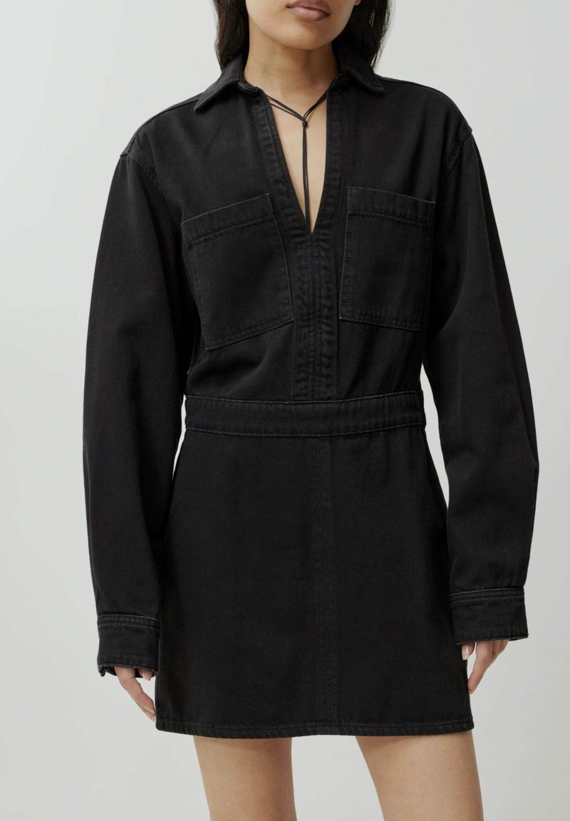 Zwarte denim jurk met lange mouwen, kraag en twee borstzakken. Kenmerkt zich door een diepe V-hals en een getailleerde taille voor een gestructureerde pasvorm.