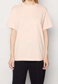 Light pink cotton t-shirt with short sleeves, crew neckline, and small white Nike logo on the chest. Relaxed fit, simple design.