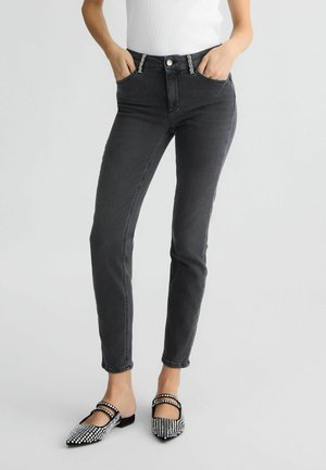 Jeans neri slim-fit con passanti decorativi, tasche anteriori e una texture liscia. Abbinati a scarpe nere con decorazioni di strass.