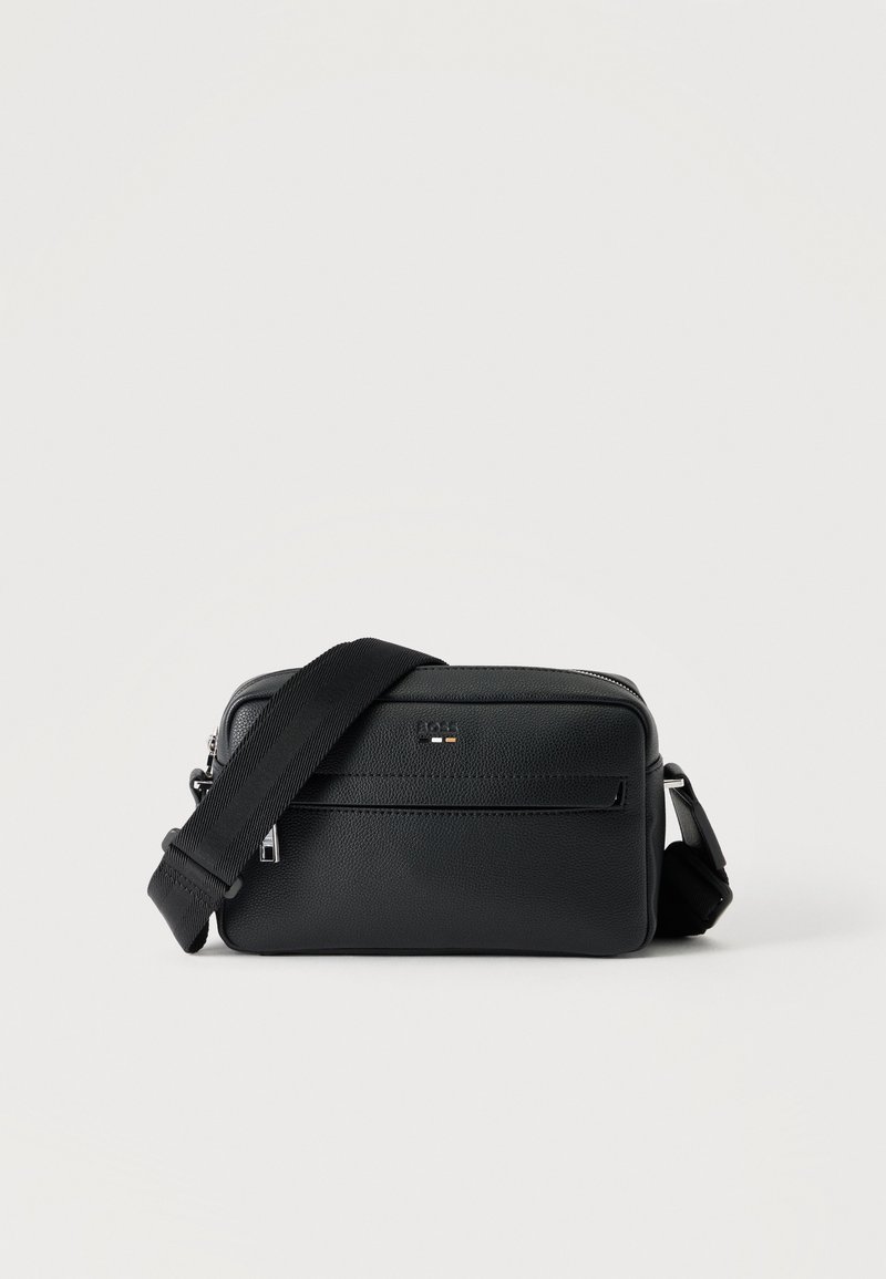 Μαύρη τσάντα crossbody από δέρμα με υφή, εμπρόσθια τσέπη με φερμουάρ και ρυθμιζόμενο φαρδύ υφασμάτινο ιμάντα ώμου, σε λευκό φόντο.