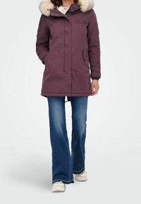 Fioletowa kurtka parka z kapturem wykończonym sztucznym futrem, zapinana na zamek z przodu, z bocznymi kieszeniami i luźnym krojem, w zestawie z rozszerzanymi dżinsami i białymi trampkami.