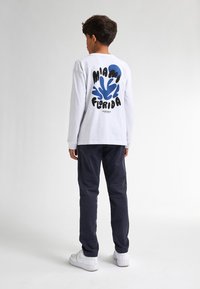Maglietta bianca a maniche lunghe con stampa grafica blu che recita "Miami Florida" sul retro, abbinata a pantaloni blu navy e sneaker bianche.