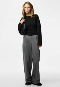 Top nero a maniche lunghe con una vestibilità rilassata, abbinato a pantaloni grigi a righe sottili, ampi e a vita alta, e a una borsa nera testurizzata.