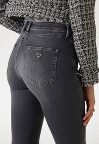 Grijze skinny jeans met een hoge tailleband, voorzien van gelogodeerde achterzakken en een gestructureerde zwart-witte cropped jas.