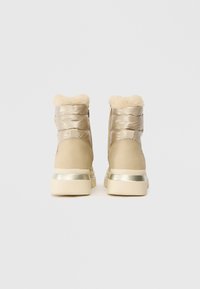 Beige winter boots with a glossy finish, faux fur collar, and metallic accents on the heel. Textured surfaces with stitched detailing.