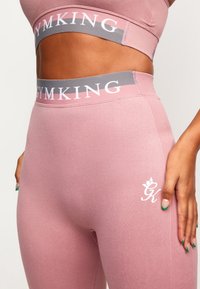 Růžové sportovní legíny s texturovaným povrchem, šedý pás se sadou "GYMKING" a bílý detail loga na stehně.