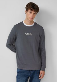 Graues Langarmshirt mit runder Ausschnitt, mit weißem gesticktem Logo "s.Oliver Co. Established 1969" auf der Brust. Klassischer Schnitt.