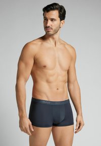 Pánské boxerky tmavě šedé barvy vyrobené z elastické tkaniny. Mají přiléhavý střih, měkkou texturu a elastický pás se značkováním.