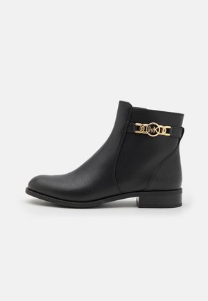 Bottine en cuir noir avec une finition texturée, bout arrondi, petit talon carré et un accent en chaîne dorée arborant le logo "MK".