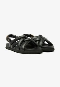 Zwarte leren sandalen met kruislingende banden en een slingback ontwerp. Beschikt over een platte zool en een kleine gouden gespaccent op de enkelband.