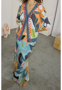 Wielokolorowy kardigan z akcentami w postaci pomponów oraz kwiatowym wzorem, w zestawie z maxi spódnicą w niebieskich tonacjach o zwiewnym fasonie.