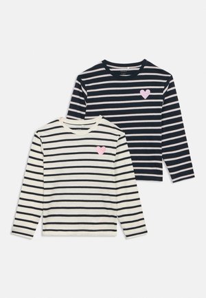 Deux chemises à manches longues à rayures, une blanche avec des rayures noires et une noire avec des rayures blanches, toutes deux ornées d'un petit cœur rose sur la poitrine.