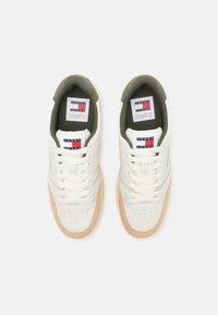 Sneaker bianche in pelle con profilo basso, suola in gomma beige chiaro, fodera in tessuto verde e lacci bianchi piatti. Presenta un marchio sulla linguetta.